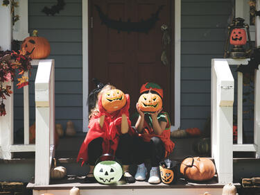 Little children in Halloween costumes sitting on steps holding pumpkins in front of their faces