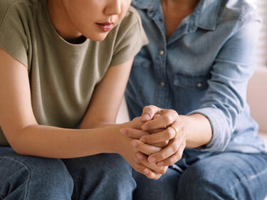 Mother holding hands with daughter, consoling the teen