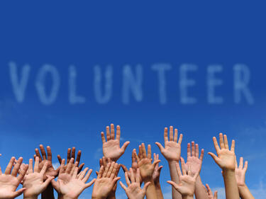 Hands raised in front of sky, volunteer written in clouds